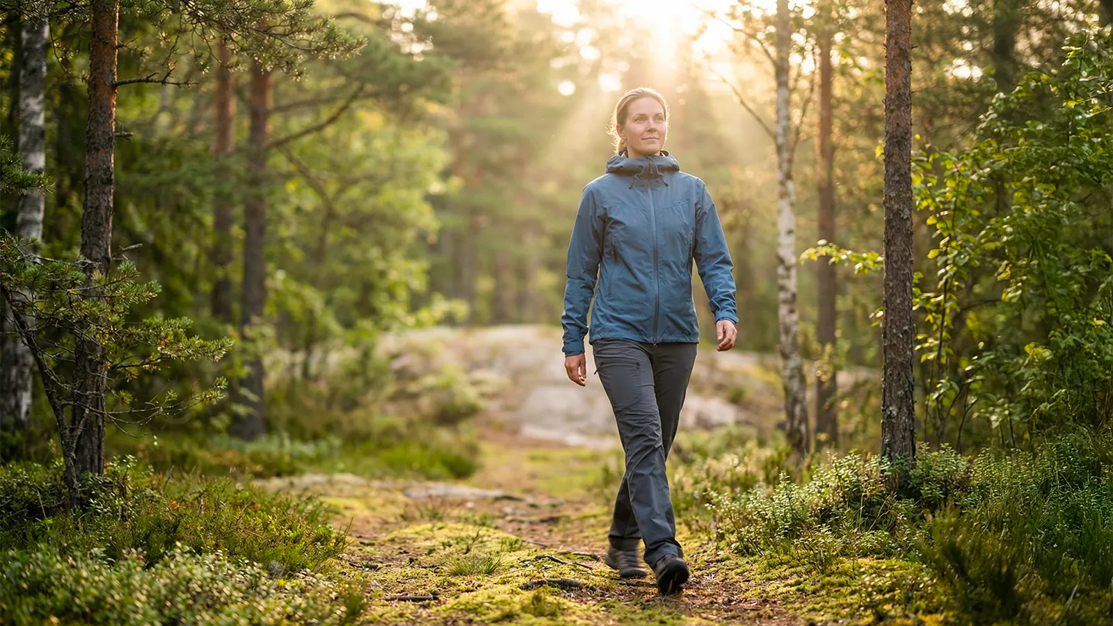 Person som promenerar i mjukt morgonljus genom skog – rörelse, energi och naturlig vitalitet