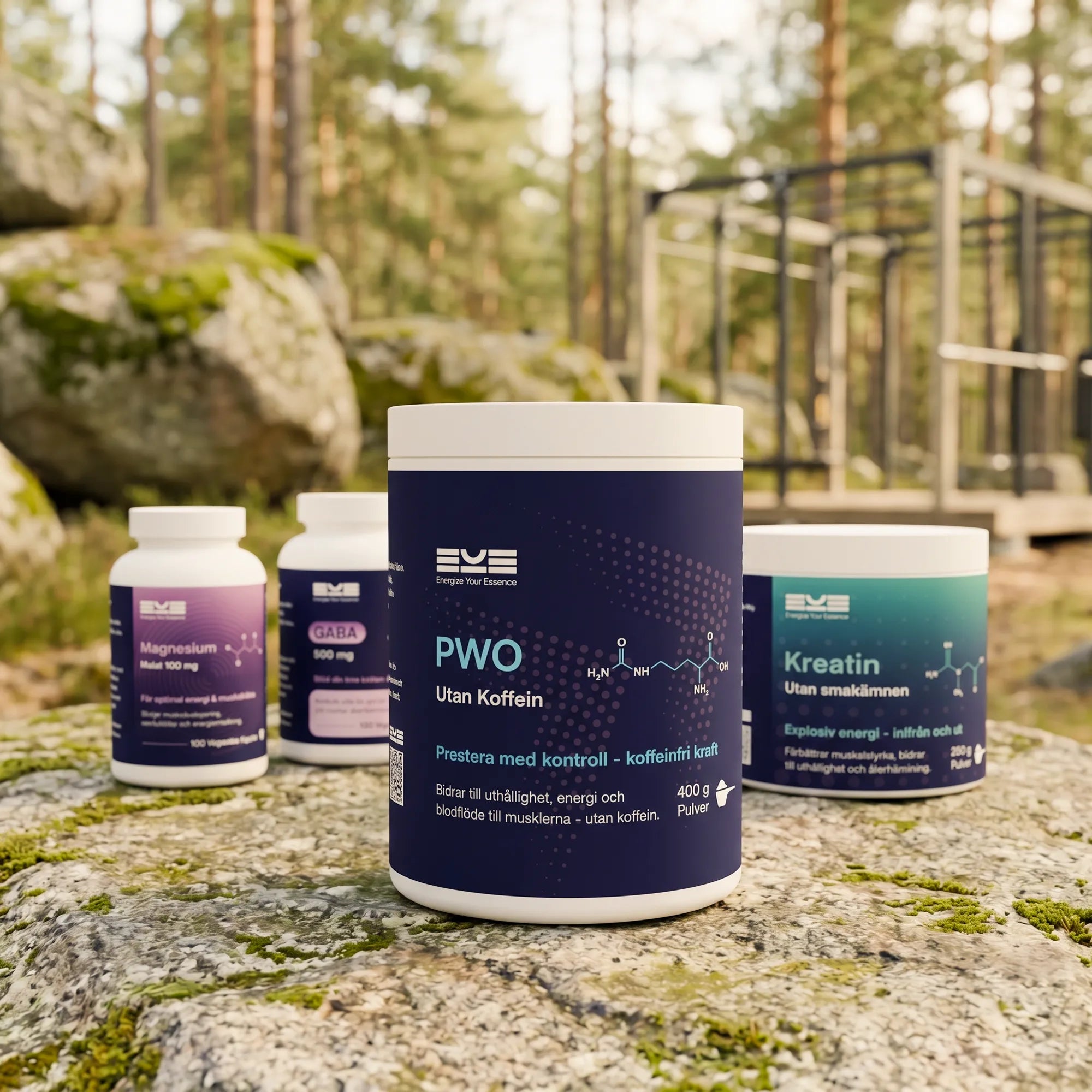 Energize Your Essence kosttillskott utomhus i skogsmiljö med PWO utan koffein, kreatin utan smak, GABA och magnesium placerade på en sten. Bakgrunden med utegym illustrerar balanserad energi, prestation och ett aktivt liv i rörelse utan koffein.