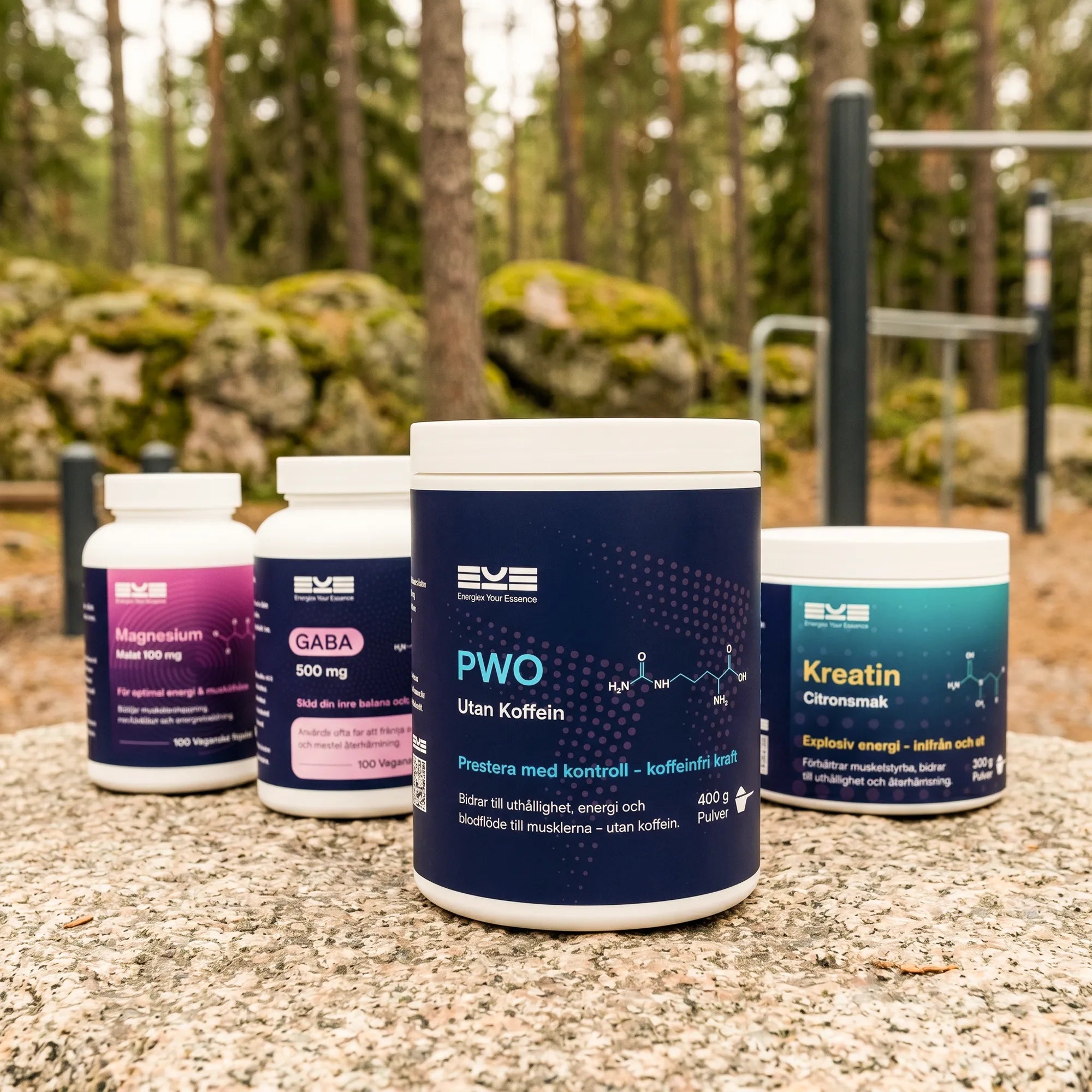 Energize Your Essence kosttillskott utomhus i skogsmiljö med PWO utan koffein, kreatin citronsmak, GABA och magnesium placerade på en sten. Bakgrunden med utegym illustrerar kontrollerad energi, prestation och ett aktivt liv i rörelse utan koffein.