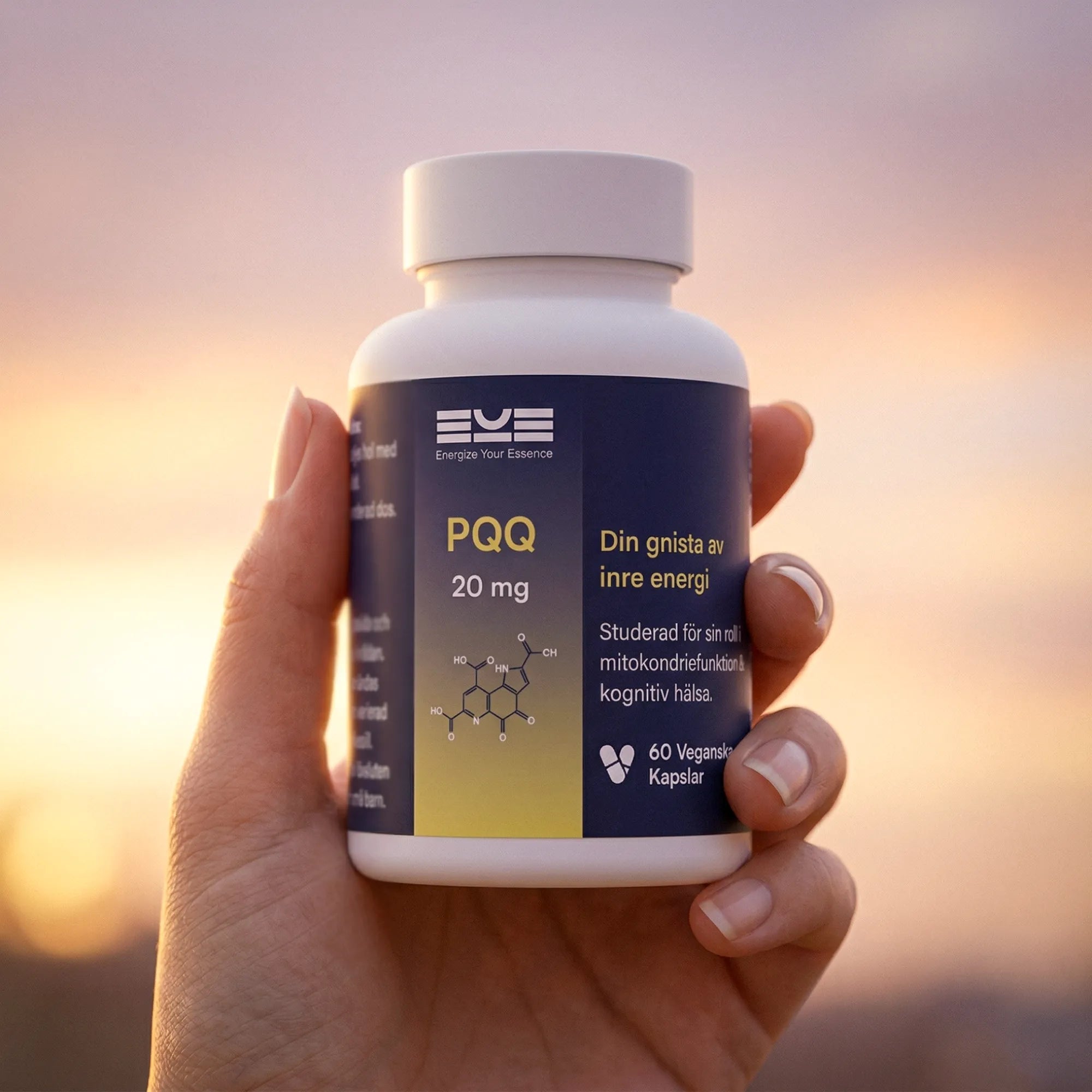 PQQ 20 mg kosttillskott från Energize Your Essence hålls i en hand i varmt kvällsljus, med suddig solnedgång i bakgrunden