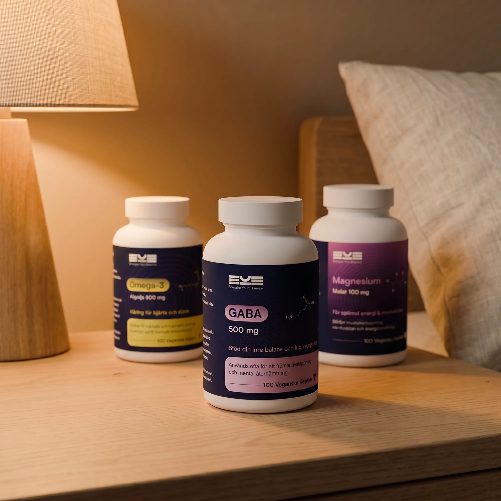 Energize Your Essence kosttillskott i sovrumsmiljö med GABA, Magnesium och Omega-3 placerade på ett nattduksbord vid en tänd lampa. Den lugna miljön illustrerar kvällsrutin, återhämtning och stöd för avslappning och sömn.