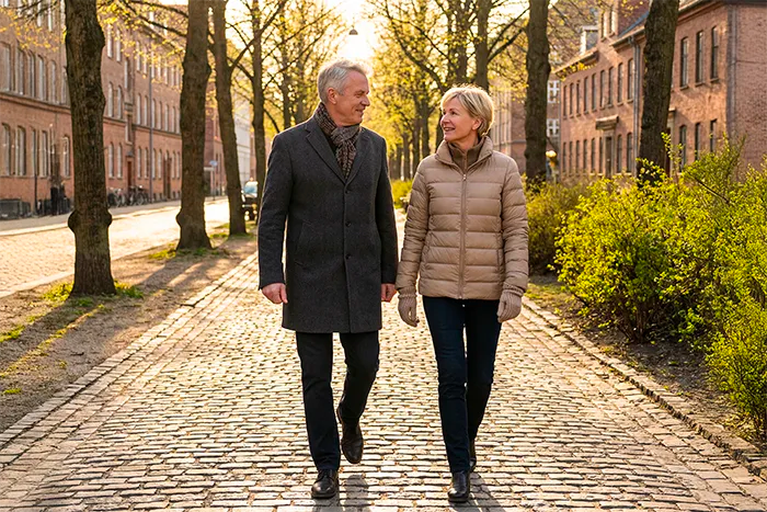Par som promenerar i stadsmiljö i varmt solljus – aktiv livsstil och långsiktigt välmående